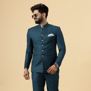 May include: A teal blue suit with a mandarin collar and button closure. The suit has a pocket square and the model is wearing brown loafers.