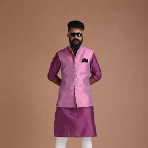 Puede incluir: Un hombre con un chaleco estampado en rosa y azul sobre una kurta morada, pantalones blancos y zapatos marrones. Lleva gafas de sol y barba.