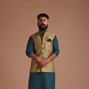 以下が含まれることがあります： 男性のフォーマルな服装。金色のブロケードベストに、ティール色のクルタと白いパンツを合わせたスタイル。ベストには繰り返し模様があり、ボタンで留められています。茶色の革靴で完成。