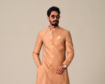 May include: A peach-colored long-sleeved kurta with a light blue and gold geometric pattern. The kurta has a mandarin collar and a button closure. The model is wearing white pants and brown loafers.
