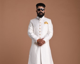 Puede incluir: Una kurta blanca de manga larga con botones dorados y un pañuelo de bolsillo dorado. La kurta se lleva con pantalones blancos y zapatos marrones.