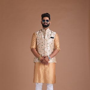 Puede incluir: Un hombre con un chaleco estampado en blanco y dorado con una kurta dorada y pantalones blancos. Lleva gafas de sol y un reloj.