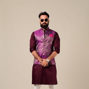 Puede incluir: Un hombre con una kurta marrón con un chaleco estampado en morado y dorado, pantalones blancos y zapatos marrones. Lleva gafas de sol y barba.