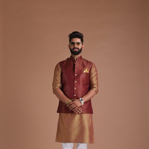 Puede incluir: Un hombre con un chaleco granate con detalles dorados sobre una kurta dorada, pantalones blancos y zapatos marrones. Lleva gafas de sol y barba.