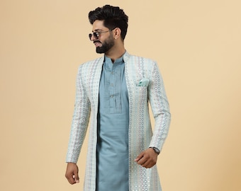 Könnte beinhalten: Ein dreiteiliges Ensemble mit einem hellblauen Kurta, passenden Hosen und einer langen, verzierten Jacke. Die Jacke hat eine weiße Basis mit einem sich wiederholenden Muster aus kleinen, farbigen Akzenten. Das Outfit wird durch braune Lederschuhe ergänzt.