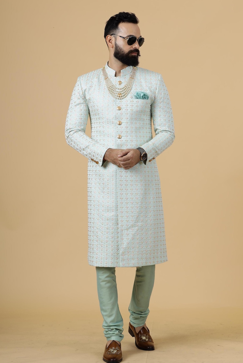 May include: A light blue patterned long-sleeved kurta with gold buttons and a gold necklace. The kurta is worn with matching light blue pants and brown shoes.