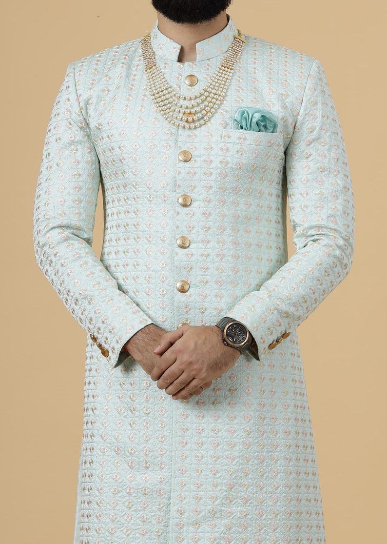May include: A light blue patterned men's sherwani with gold buttons and a pearl necklace. The sherwani has a pocket on the left side with a light blue handkerchief.