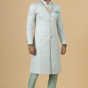 May include: A light blue patterned long-sleeved jacket with gold buttons and a pearl necklace. The jacket has a mandarin collar and a long, fitted silhouette.