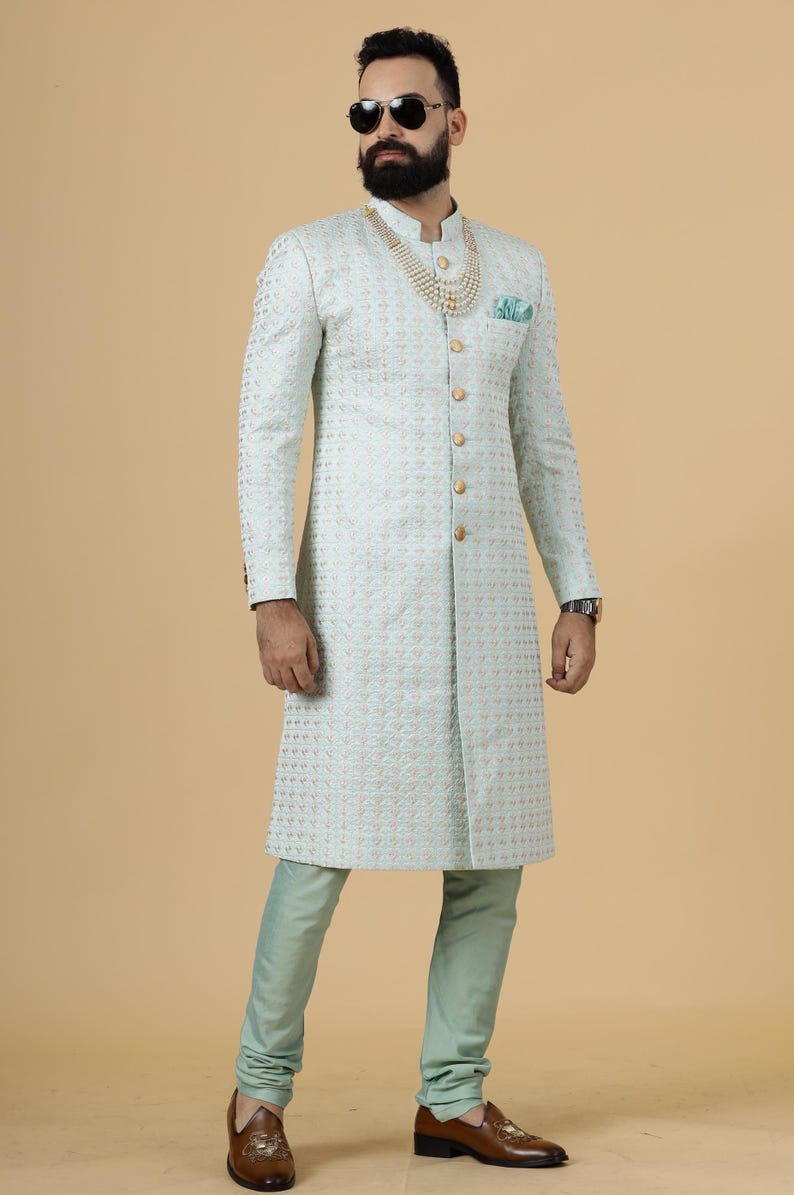 May include: A light blue patterned long-sleeved jacket with gold buttons and a pearl necklace. The jacket has a mandarin collar and a long, fitted silhouette.