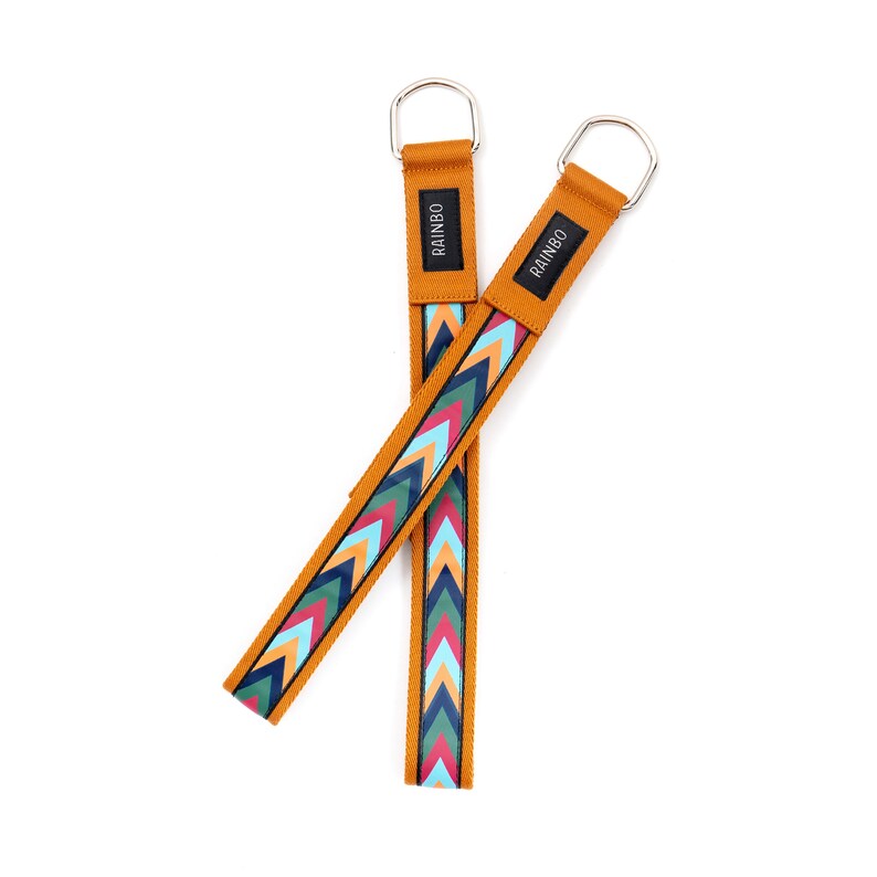 May include: Two mustard yellow straps with a colorful chevron pattern and silver metal loops. The straps have the word "RAINBO" printed on them.
