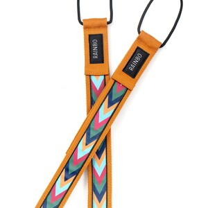 May include: Two mustard yellow camera straps with a chevron pattern in shades of blue, pink, and green. The straps have a black loop at the top and the word "RAINBO" printed on the strap.