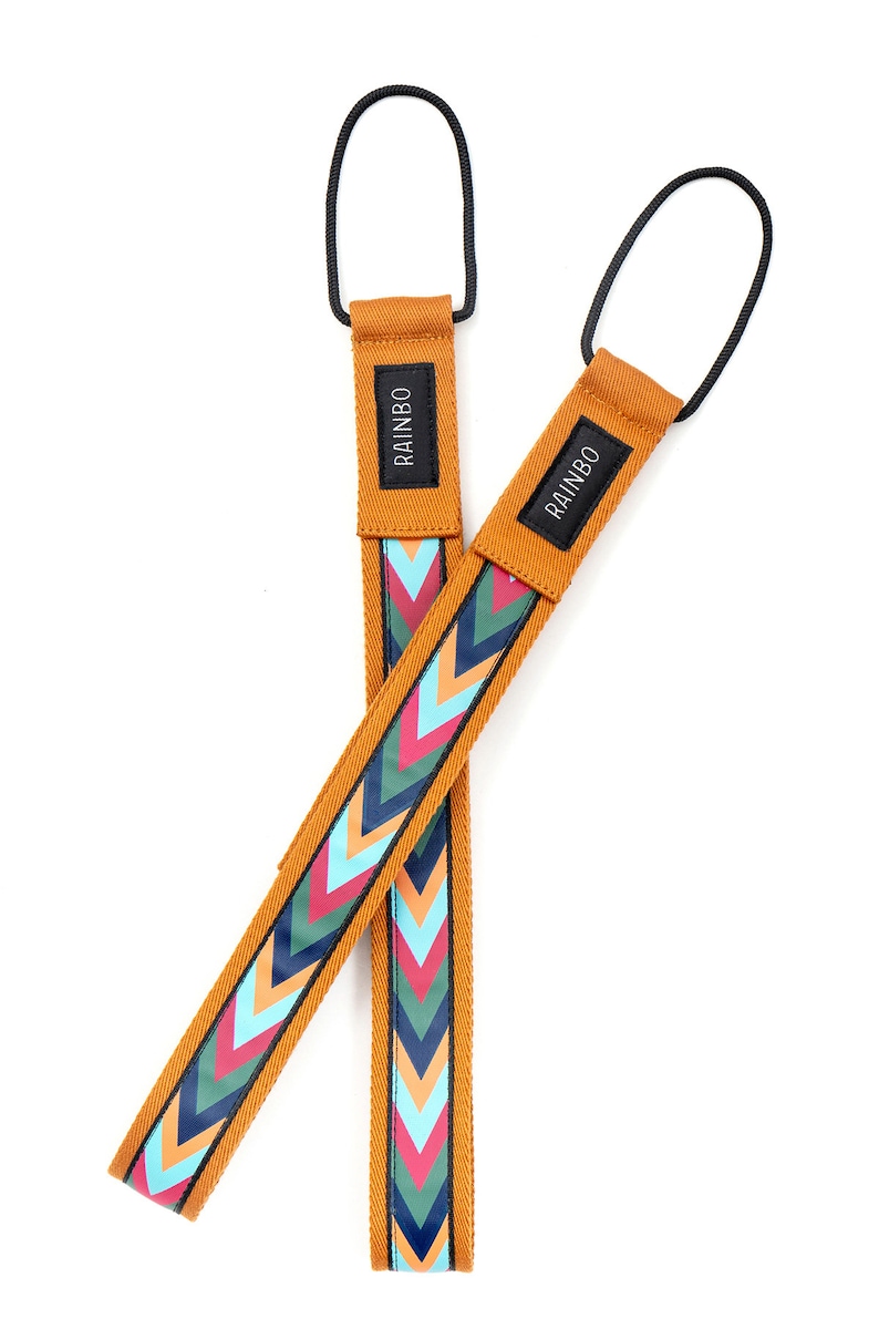 May include: Two mustard yellow camera straps with a chevron pattern in shades of blue, pink, and green. The straps have a black loop at the top and the word "RAINBO" printed on the strap.