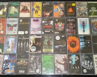 May include: A collection of 30 cassette tapes in clear plastic cases. The tapes are arranged in rows of five. The tapes feature a variety of bands and artists, including Adema, Papa Roach, Coal Chamber, and Crazy Town. The tapes are all in good condition and have been well-cared for.