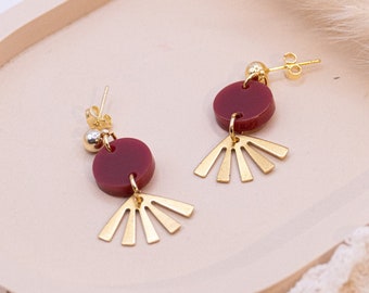 May include: A pair of gold earrings with a burgundy circle and gold fan-shaped accents.