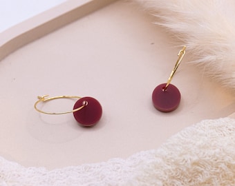 May include: A pair of gold hoop earrings with a burgundy round charm attached to each hoop.