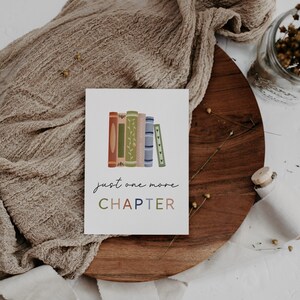Peut inclure: Une carte blanche avec une pile de livres color&eacute;s et le texte "just one more CHAPTER" en &eacute;criture cursive noire.