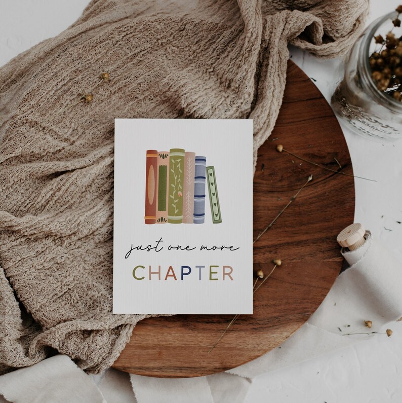 Peut inclure: Une carte blanche avec une pile de livres color&eacute;s et le texte "just one more CHAPTER" en &eacute;criture cursive noire.