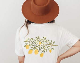 May include: White t-shirt with a lemon branch design printed on the back. The branch has green leaves and yellow lemons.