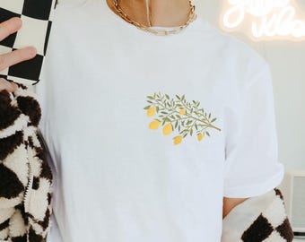 May include: White t-shirt with a lemon branch graphic. The lemons are yellow and the leaves are green.