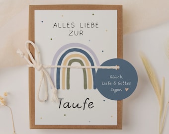 Könnte beinhalten: Eine weiße Karte mit einem Regenbogen-Design und dem Text "Alles Liebe zur Taufe" in Schwarz. Ein blauer runder Anhänger mit dem Text "Glück, Liebe & Gottes Segen" ist mit einer weißen Schnur an der Karte befestigt.