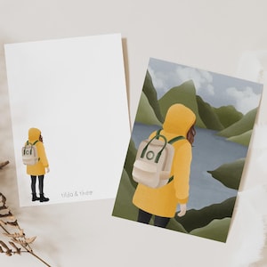 Può includere: Due stampe artistiche raffiguranti una persona con impermeabile giallo e zaino. Una stampa mostra la persona in piedi, l'altra mostra la persona che si affaccia su un lago e montagne. Le stampe hanno il testo "tilda & theo".
