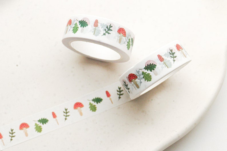May include: Two rolls of white washi tape with a repeating pattern of red and white mushrooms, green leaves, and white stems.