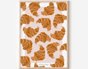 May include: A framed print featuring a pattern of watercolor croissants in shades of brown against a light pink background. The print has a wooden frame and the text "tilda & theo" is in the bottom right corner. The image is a food-themed illustration.