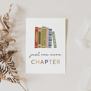 Peut inclure: Une carte blanche avec une pile de livres color&eacute;s et le texte "just one more CHAPTER" en lettres color&eacute;es.