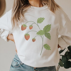 May include: White sweatshirt with a graphic of a strawberry plant with green leaves and red strawberries.