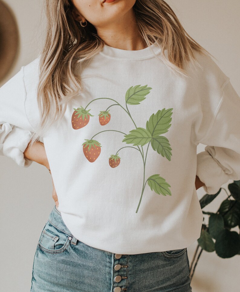 May include: White sweatshirt with a graphic of a strawberry plant with green leaves and red strawberries.