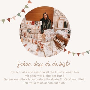 Peut inclure: Une femme se tient derri&egrave;re une table remplie d'articles faits &agrave; la main, notamment des cartes, des autocollants et d'autres articles en papier. La table est d&eacute;cor&eacute;e d'une guirlande de drapeaux festive. Le texte sur l'enseigne indique "Sch&ouml;n, dass du da bist!" qui se traduit par "C'est bien que vous soyez l&agrave; !"