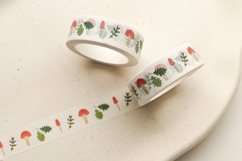 May include: Two rolls of white washi tape with a repeating pattern of red mushrooms and green leaves.
