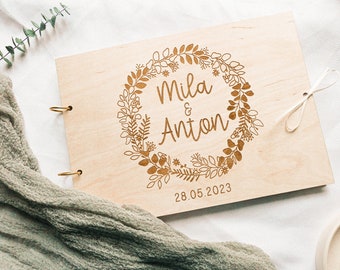 May include: A wooden photo album with a floral wreath design and the names Mila & Anton, and the date 28.05.2023 engraved on the front cover.