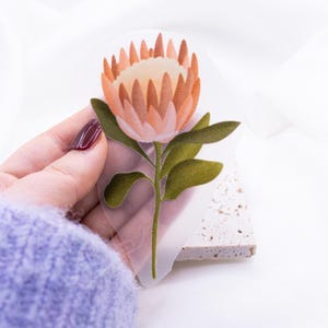 May include: A clear sticker with a pink and orange protea flower with green leaves.