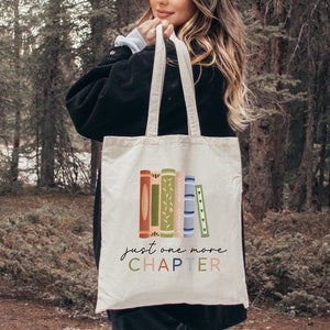 May include: A white canvas tote bag with a colorful illustration of stacked books and the text "just one more CHAPTER".