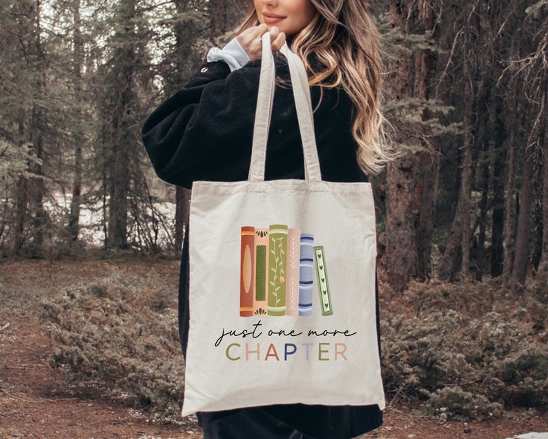 May include: A white canvas tote bag with a colorful illustration of stacked books and the text "just one more CHAPTER".