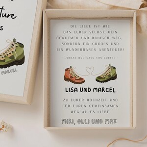 May include: A white card with a quote about love being an adventure, illustrated with two hiking boots tied together with a heart-shaped string. The card reads "Lisa und Marcel" and "Zu eurer Hochzeit und fur euren gemeinsamen Weg alles Liebe. Miri, Olli und Max."