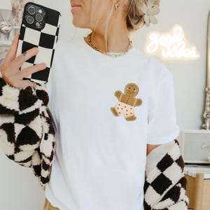 Könnte beinhalten: Weißes T-Shirt mit einem Lebkuchenmann, der eine braune Hose mit rosa Herzen trägt.