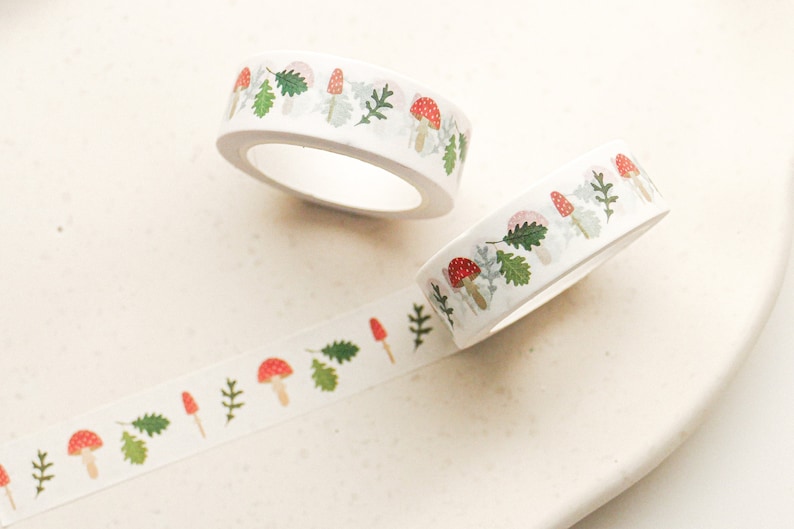 May include: Two rolls of white washi tape with a repeating pattern of red and white mushrooms and green leaves.
