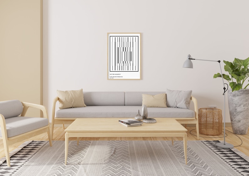 May include: A black and white abstract geometric print in a wooden frame hangs on a white wall above a light gray sofa with beige pillows. A wooden coffee table sits in front of the sofa with a book and two decorative objects on top. A floor lamp with a gray shade and a potted plant are on the right side of the image. A patterned rug is on the floor.