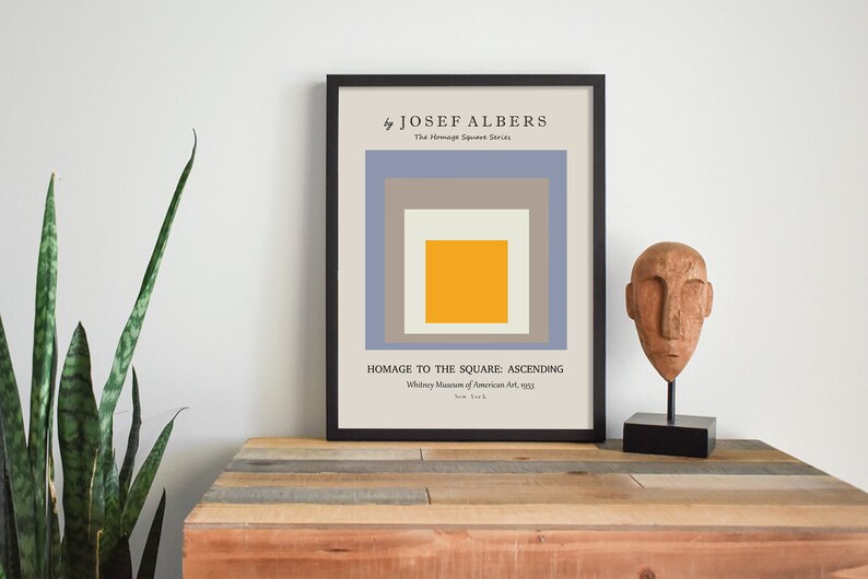 May include: A framed print of a geometric abstract art piece by Josef Albers titled "Homage to the Square: Ascending". The print features a series of squares in shades of blue, grey, and yellow.