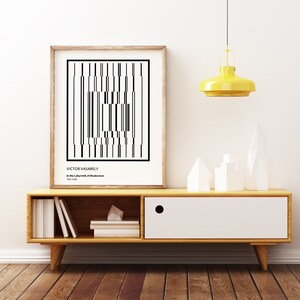 May include: A black and white geometric art print by Victor Vasarely titled "In the Labyrinth of Modernism" (1963-1965) framed in a natural wood frame and displayed on a wooden shelf with white geometric decor.