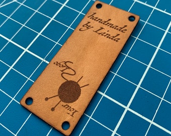May include: A brown leather tag with the text "handmade by Linda" and a stylized illustration of a ball of yarn with knitting needles.