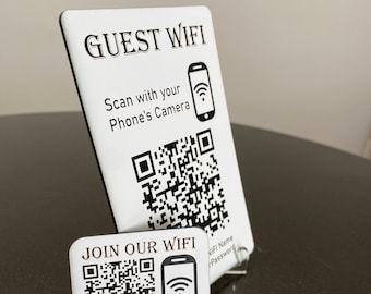 May include: White sign with black text that reads "GUEST WIFI" and instructions to scan with your phone's camera. A black and white QR code is below the text. A smaller white sign with black text that reads "JOIN OUR WIFI" and a black and white QR code is below the text. The text also reads "WiFi Name Password" and "SSID: Your WiFi Name Pwd: YourPassword".