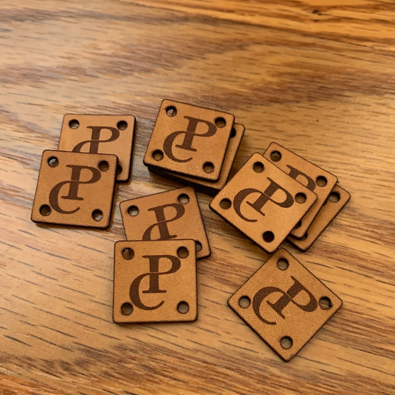 May include: A group of ten brown leather squares with a single hole in each corner. Each square has the letter "P" with a small "C" inside the "P" engraved in the center.