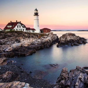 May include: A white lighthouse with a black roof stands on a rocky outcropping overlooking a calm body of water. The sky is a soft pink and blue, creating a serene and picturesque scene.