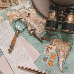 May include: A vintage world map with a magnifying glass, a pair of binoculars, a key, a pen, and a pink envelope. The map is faded and has a blue and green color scheme. There are several stamps on the map.