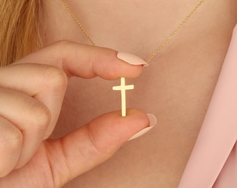 Puede incluir: Un collar de cadena de oro con un pequeño colgante de cruz de oro simple.