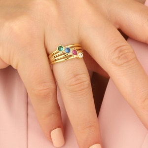 May include: Gold ring with four small colorful gemstones. The ring is stacked with three other gold bands.