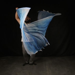 May include: A person wearing a white shirt and grey trousers is holding a blue and white fabric in their hands. The fabric is flowing in the air.